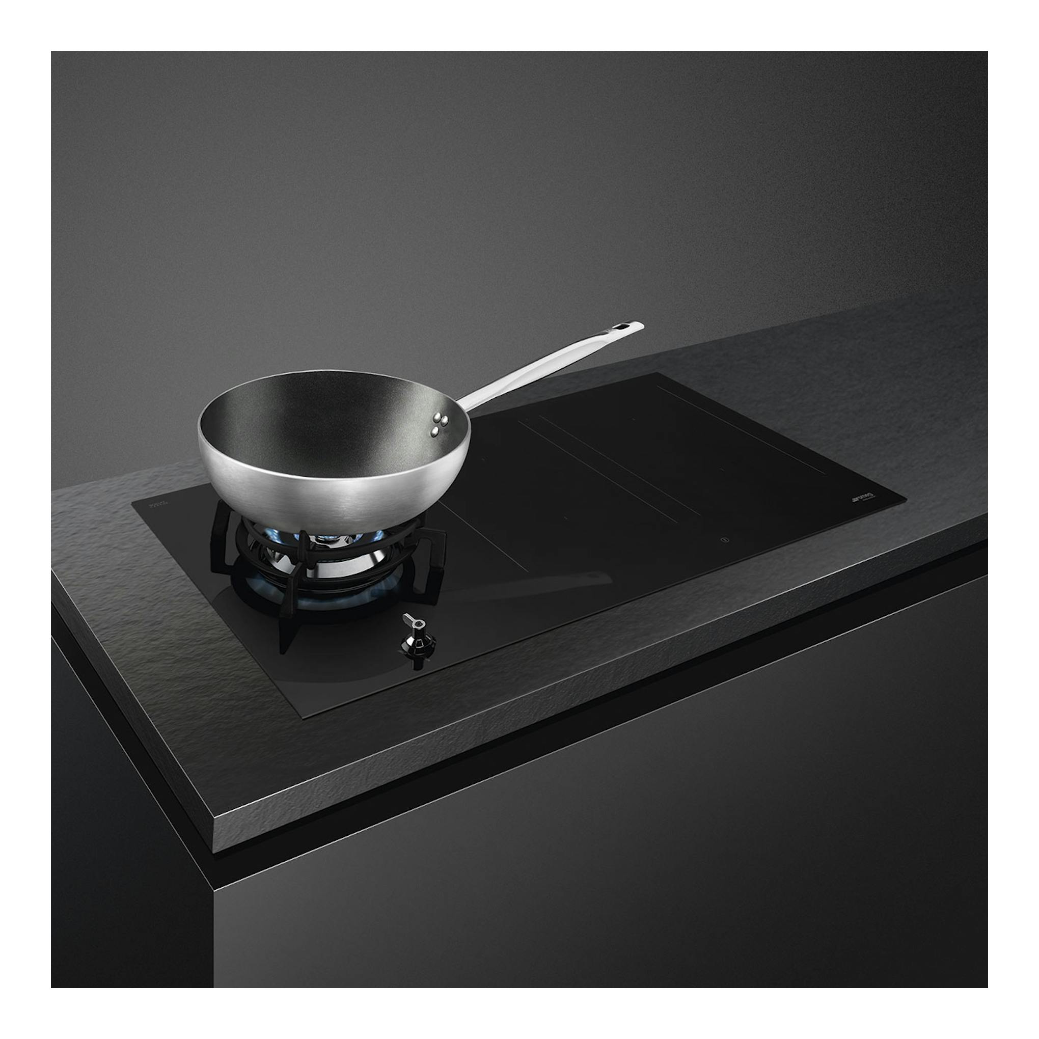 Placa mixta Smeg PM3953D negra, vista en ángulo, con wok sobre quemador de gas y zona de inducción.