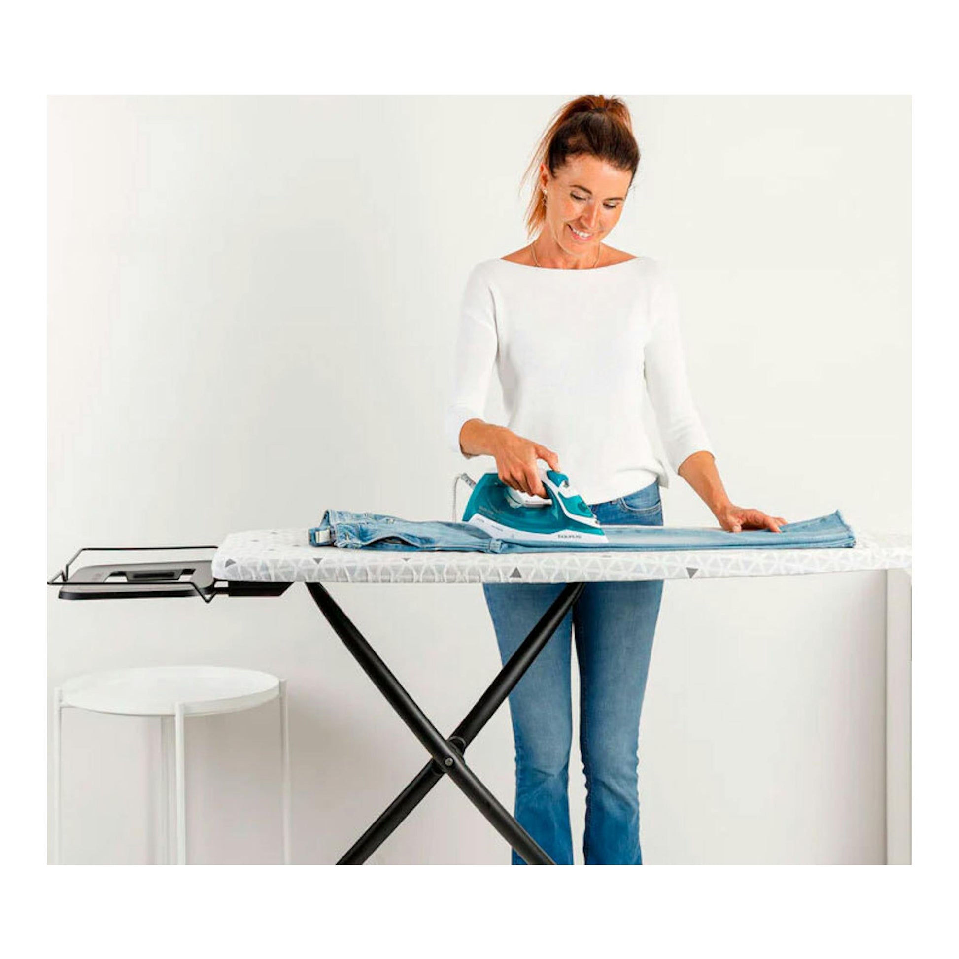 Plancha de vapor Taurus Baltic 2400 turquesa sobre tabla de planchar, con una mujer planchando unos vaqueros.