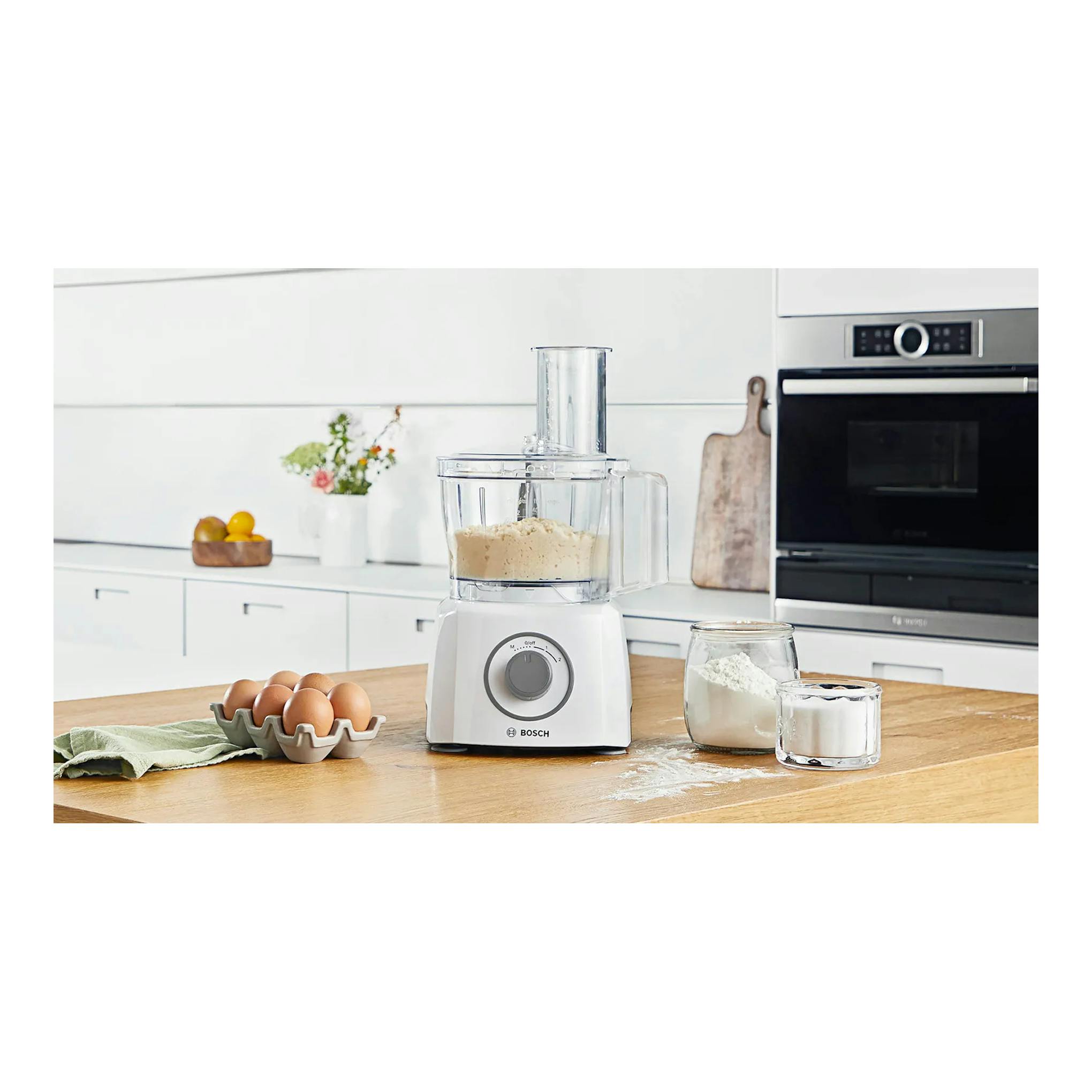 Procesador de alimentos Bosch MultiTalent 3 blanco, vista frontal, con masa en el bol sobre una encimera.