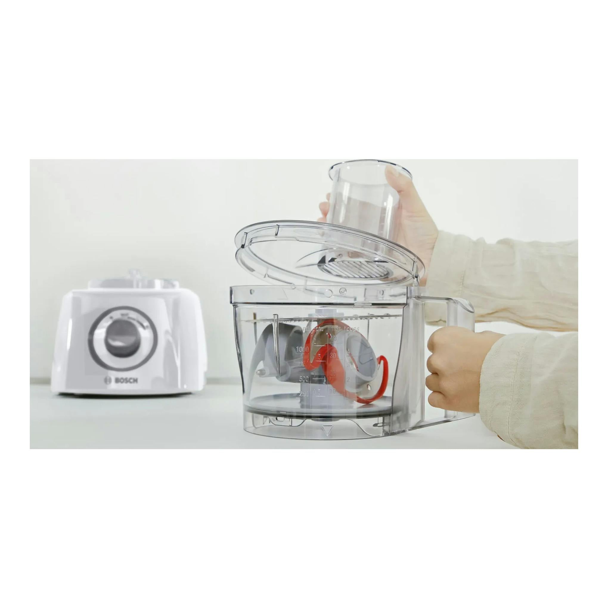 Procesador de alimentos Bosch MultiTalent 3 MCM3100W blanco, con cubeta transparente y mano sosteniendo accesorio.