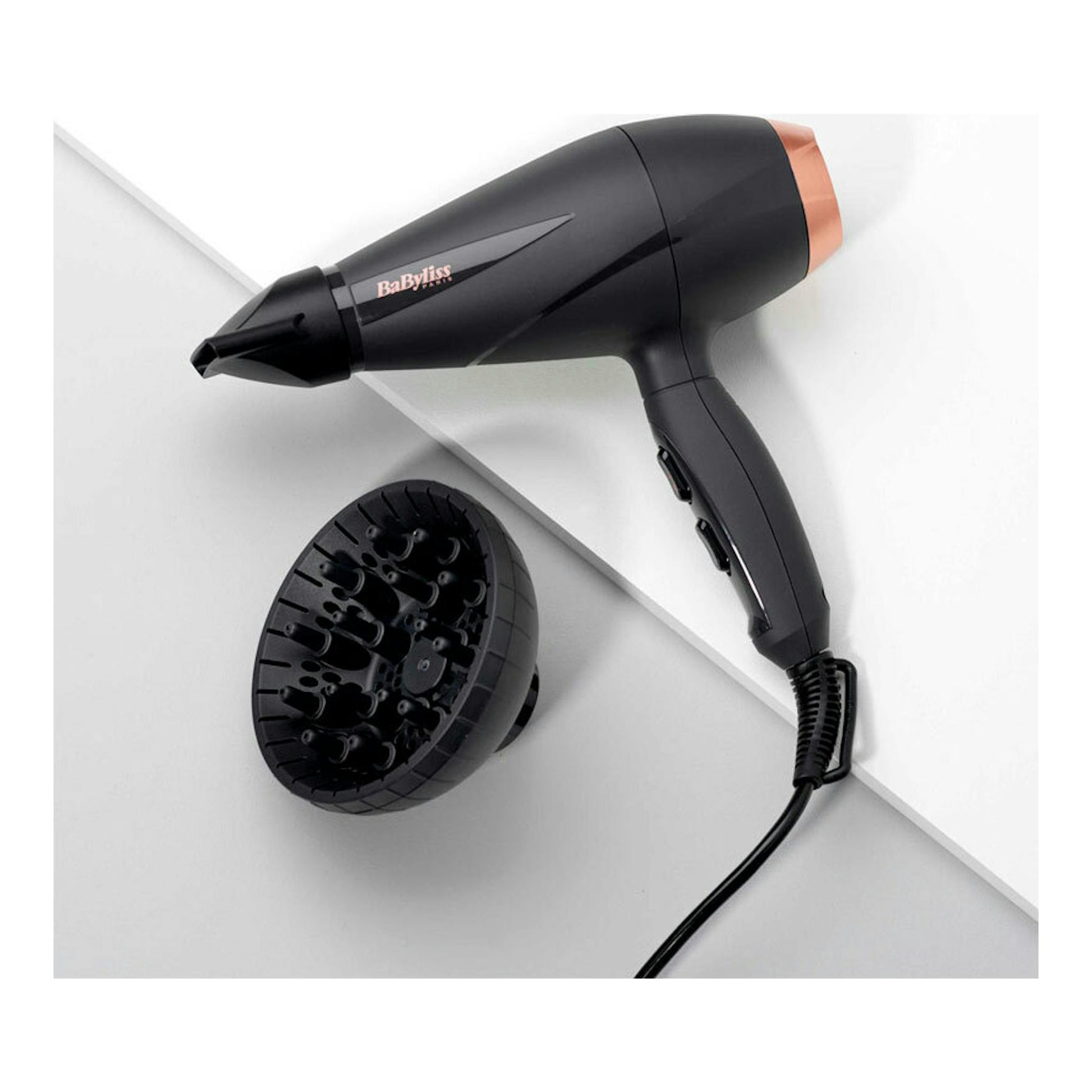 Secador Babyliss 6709DE negro con detalles cobre, vista lateral, con boquilla y difusor sobre fondo blanco.