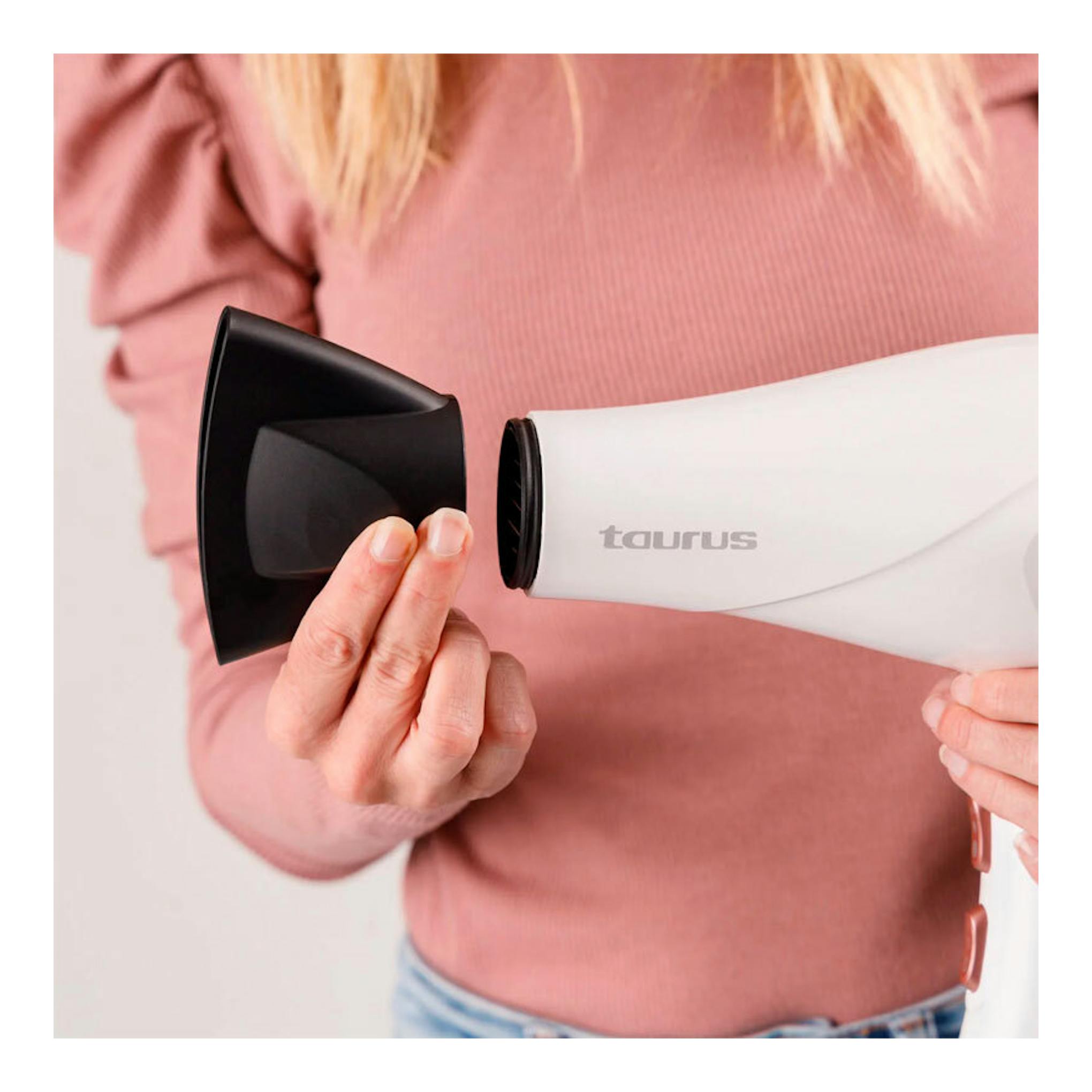 Secador Taurus Fashion 2600 Ionic blanco con difusor negro, sostenido en primer plano por una persona.