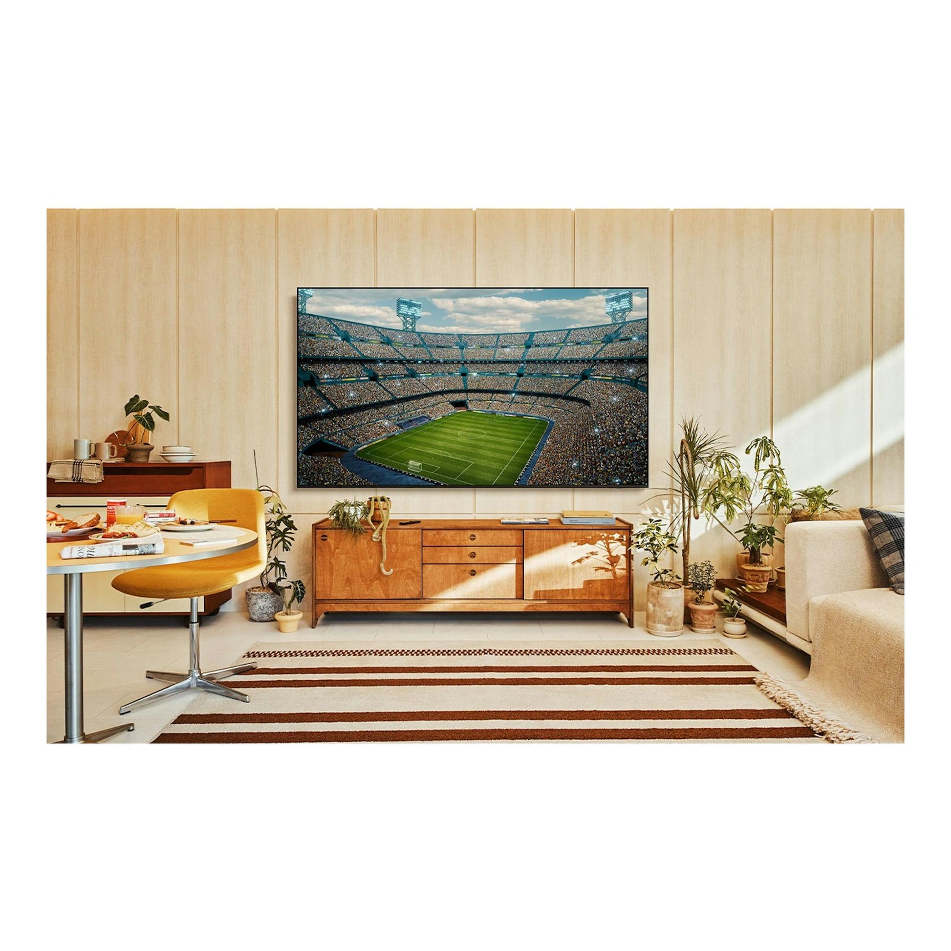 Samsung TU75U7005FKXXC, televisor negro en vista frontal en un salón, con un estadio de fútbol en pantalla.