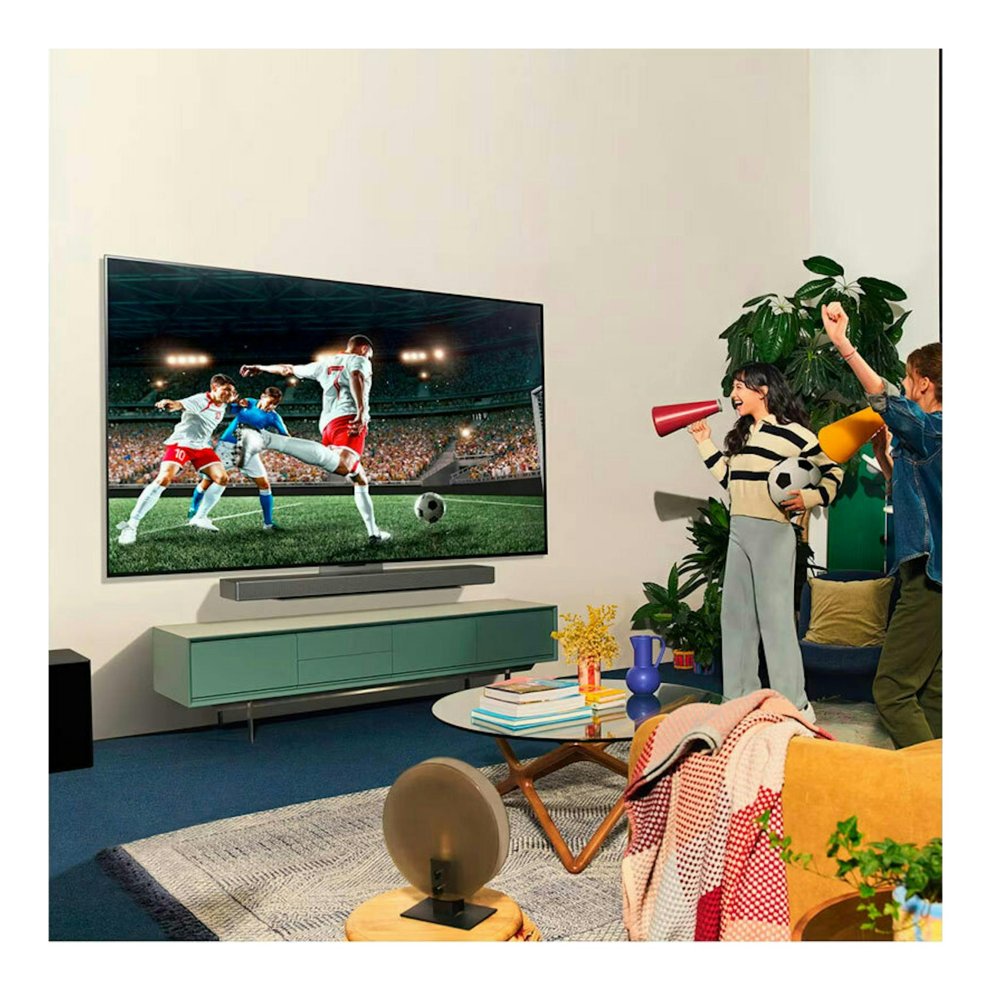 TV LG OLED55C44LA.AEU de pared en salón, mostrando un partido de fútbol y una barra de sonido debajo.