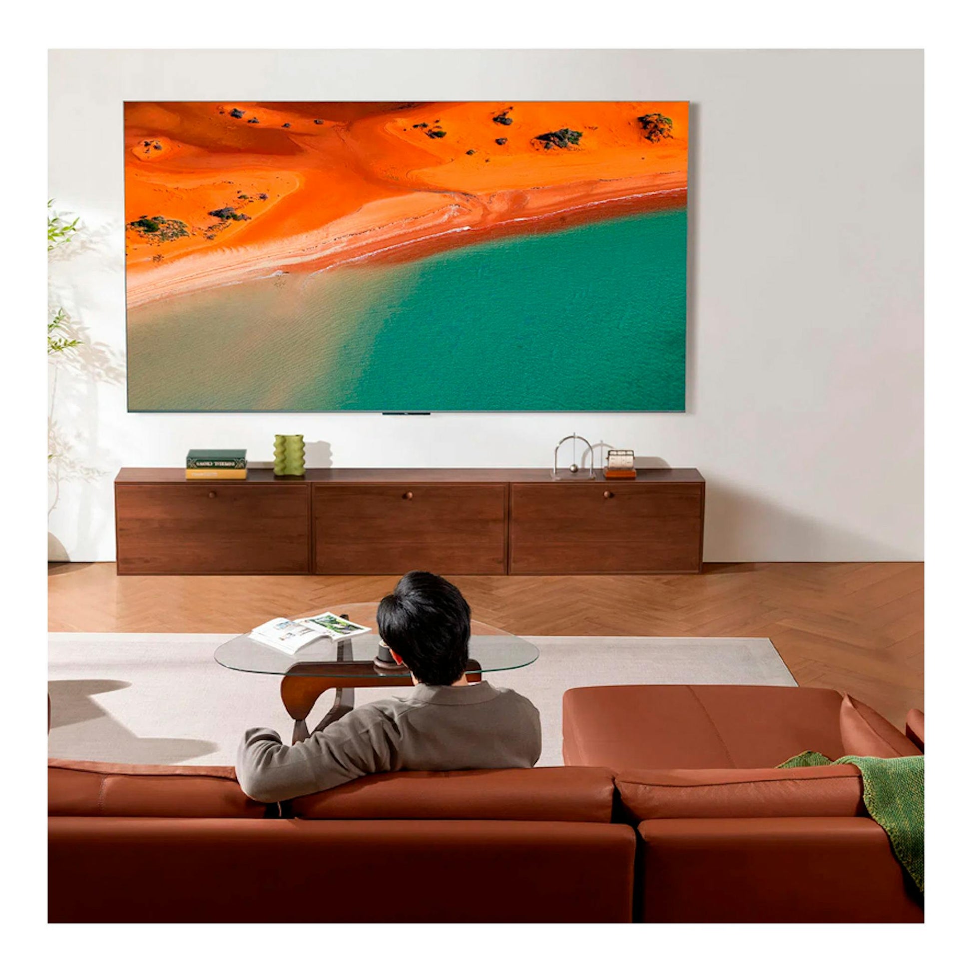Televisor TCL 75C8K negro, vista frontal en pared, con imagen de costa naranja y mar turquesa.