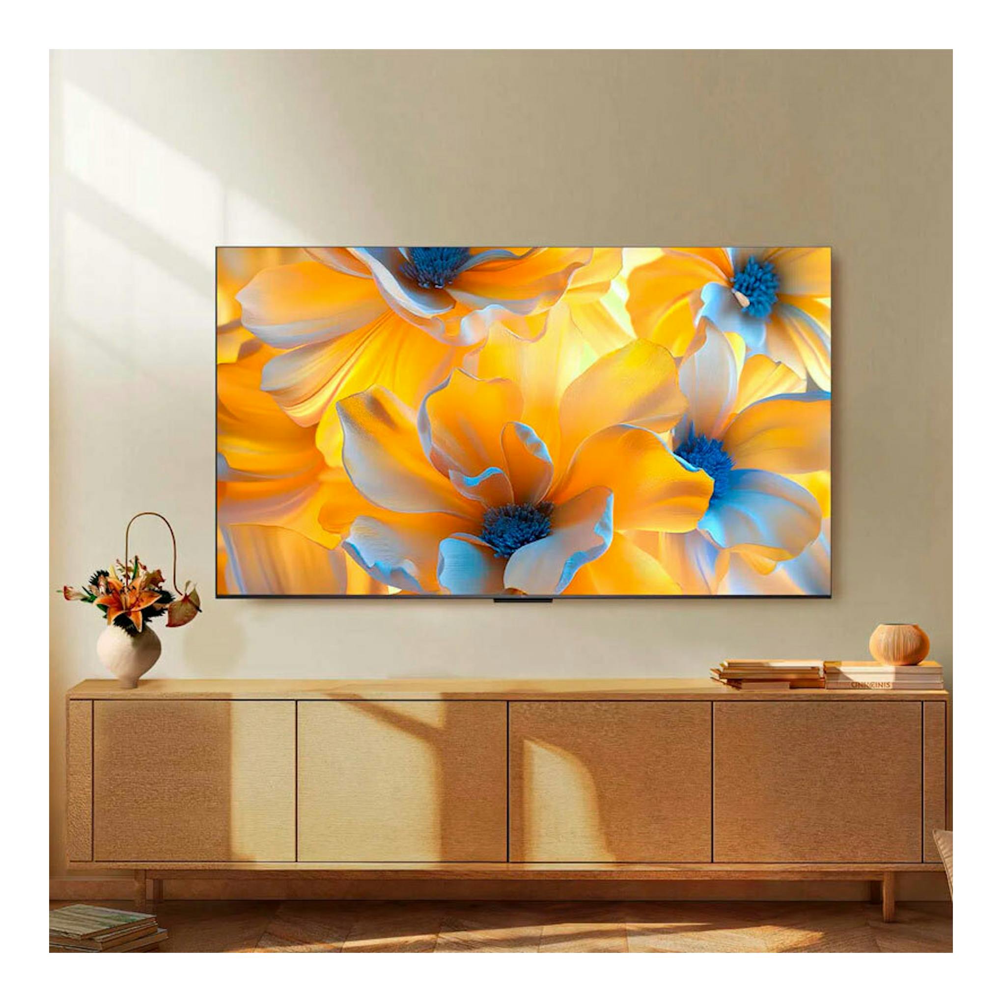 Televisor TCL 85C6K de 85" montado en la pared, vista frontal, con pantalla mostrando flores amarillas y azules.